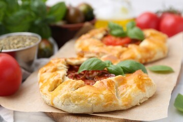 Tasty galettes with tomato and basil on white tiled table, closeup