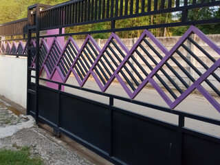 A modern, minimalist sliding gate with a black frame and purple accents in front of a green bamboo...