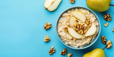 Healthy breakfast: A bowl of porridge topped with pear slices and walnuts on a blue background. Flat lay. Copy space. Top view.