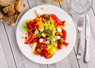 Healthy fresh salad of lettuce, red sweet pepper, tomato, corn, olives, onion and soft cheese with pesto dressing