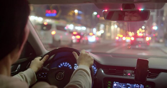 A captivating nighttime scene unfolds as seen from inside a car, revealing vibrant and illuminated city streets while highlighting the drivers calm demeanor and safe navigation as they proceed ahead