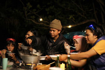 Friends Cooking Together While Camping at Night Outdoors