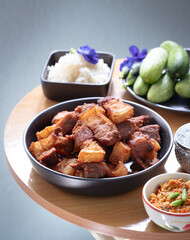 Deep fried sliced crispy pork belly in a black paste with chili sauce with assorted vegetables in background such cucumber and butterfly pea flower. 