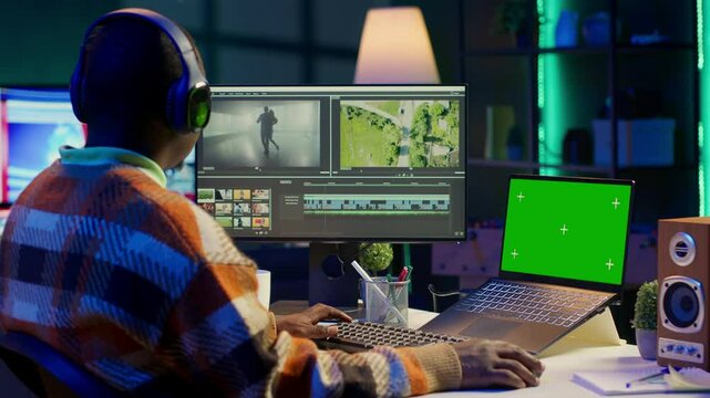 African american man editing film footage on his dual monitors, create content for cinematography next to copy space. Workspace organized for productivity, editing software and multitasking. Camera A.