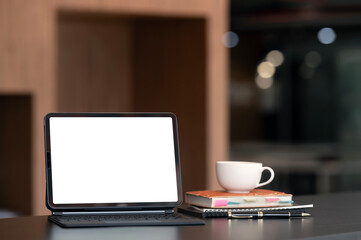 Digital tablet blank screen on the desk with coffee and book pencils at the office.