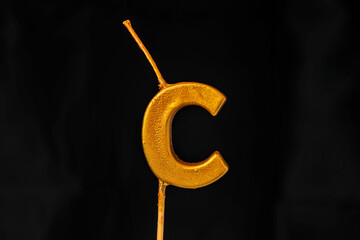 close up on gold Letter C birthday candle on a dark background.
