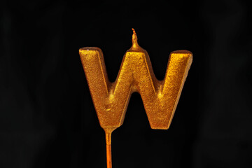 close up on gold Letter W birthday candle on a dark background.
