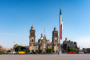 Mexico City Metropolitan Cathedral with a Large Mexican Flag in Zocalo Square, Showcasing Historic Architecture and National Symbolism Under a Clear Blue Sky on a Sunny Morning