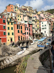 Colorful hillside houses of Riomaggiore in Cinque Terre, Italy, with small boats lining the harbor and stone pathways. A lively and picturesque scene blending coastal charm and Italian architecture.