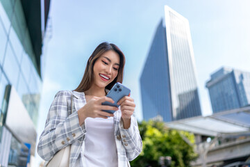 Fototapeta premium Asian Businesswoman Using Phone In Front of Cityscape Background