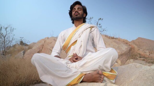 young Indian yogi doing his yoga mediation practices on hills rocks in forest