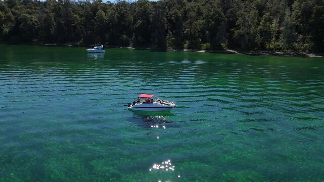 boat with a red canopy floating on the pristine, emerald-green waters of Bah&iacute;a Lynch, located in the Arrayanes Forest, within Nahuel Huapi Lake. Surrounded by lush vegetation and calm waters