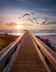 Wooden pier stretching towards a vibrant sunset, birds in flight overhead.