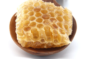 A close-up view of a piece of honeycomb on a wooden spoon, set against a white background
