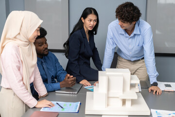 Architects engineers collaborating on building design project in modern office, diverse team of professionals female muslim architect and male engineers discussing architectural model of structure