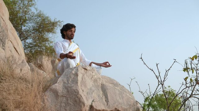 young Indian yogi doing his yoga mediation practices on hills rocks in forest