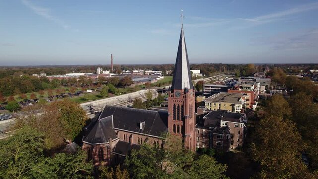 Parish St. Antonius of Padua church in Dutch town Nijverdal seen from above on a sunny day with the tower rising above countryside landscape and train station tunnel in the background