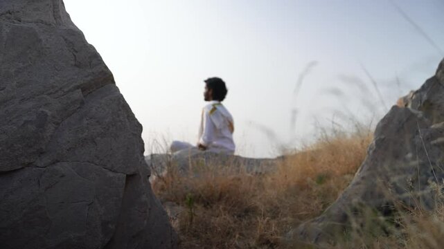 young Indian yogi doing his yoga mediation practices on hills rocks in forest