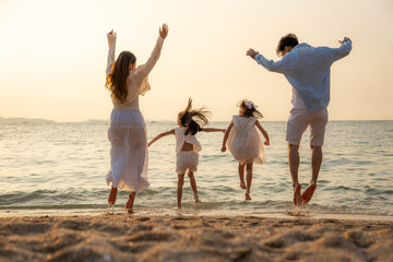 Happy Asian family on holiday vacation.  Father, Mother with two children enjoying  jumping together on the beach