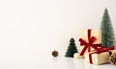Minimalistic side view scene with Christmas gifts wrapped in brown paper and red ribbons, surrounded by small pine trees on a white background