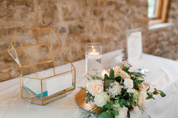 Glass box with cards on the table at the wedding, close-up. A wedding box with gold elements stands on a table decorated with flowers and candles for cards, wishes from guests for the bride and groom