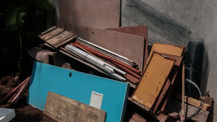 A chaotic pile of discarded building materials wood scraps, plywood, wire mesh, and a teal panel...