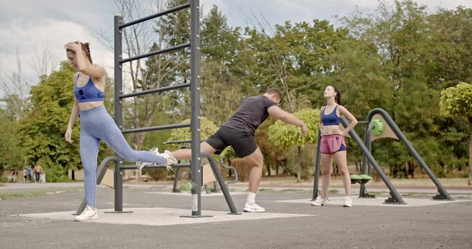 Young people working out and improving their fitness using outdoor gym equipment in a green park