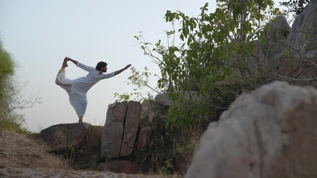 young Indian yogi doing his yoga mediation practices on hills rocks in forest