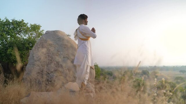 young Indian yogi doing his yoga mediation practices on hills rocks in forest