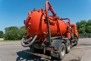 Sewage truck with an orange tank on the road