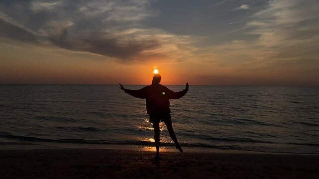 The silhouette of a girl dancing on the sand against the background of sunset and the horizon of the sea. 4k video. High quality 4k footage.