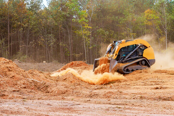 Powerful bulldozer is actively pushing dirt debris at construction site surrounded by trees dust...