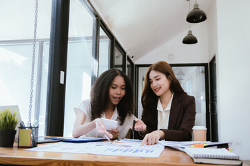 Two Asian businesswomen in suits talking at work, discussing chart analysis, business investment.