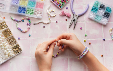 Child making beaded bracelets at home on pink tiled table