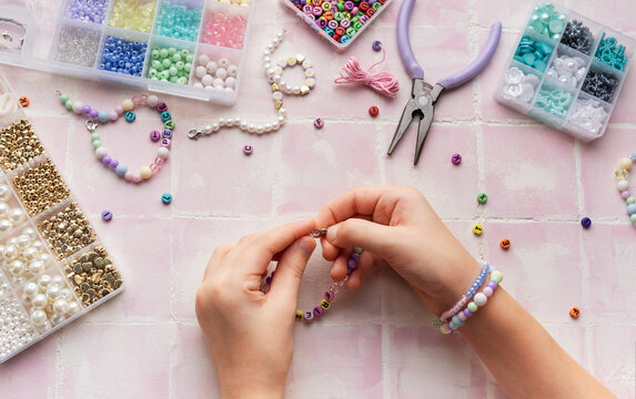 Child making beaded bracelets at home on pink tiled table