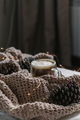 New Year, Christmas card. Coffee with milk in a glass mug among the cones on the blanket. Vertical photo