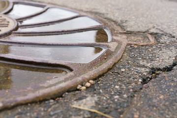 Rusty metal grate is sitting on a wet road puddle