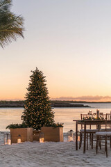 Fototapeta premium A Christmas tree on the beach with a table set for dinner. AI.