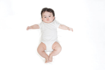 白いロンパースを着て仰向けに寝るカメラ目線の赤ちゃんを俯瞰撮影