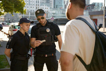 Fototapeta premium Patrol policeman and policewoman checking personal documents of citizen