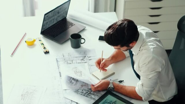 Architect engineer using laptop planning house design at office while sitting at meeting table with blueprint and equipment scatter around.Skilled civil engineer working at blueprint. Alimentation.