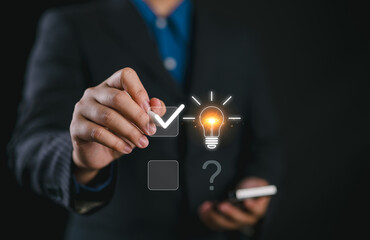 Businessman using pen to tick correct sign mark on glowing light bulb for creative thinking problem solving solution and innovation concept.