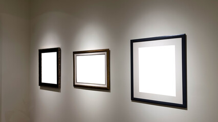 hree empty picture frames of different designs and sizes mounted on a white wall, illuminated by...