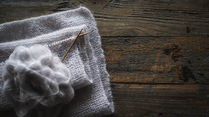 Light grey mohait wool knitting project with needles foldered on a dar rustic wooden table - hobby concept