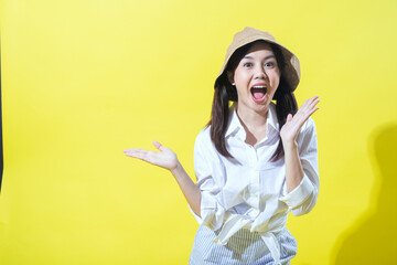 An Asian woman wearing a beige hat, white shirt, and striped pants enthusiastically poses against a...