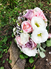 Elegant wedding bouquet with roses on rustic tree stump outdoors