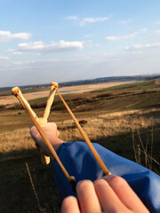Fototapeta premium Close-up of hand aiming wooden slingshot in sunny landscape