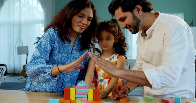Indian Asian young married couple enjoying quality time with their adorable daughter, building a home using colorful wooden block toys at a table in their modern home