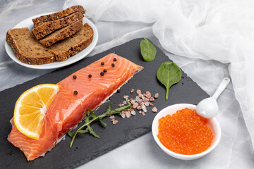 Fillet of raw salmon fish with arugula, basil and lemon on the cutting board with red caviar.