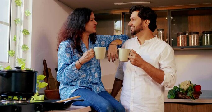 Indian couple in the kitchen - Young beautiful wife and handsome husband enjoying coffee together while sitting on the kitchen platform, chatting and sharing a joyful moment